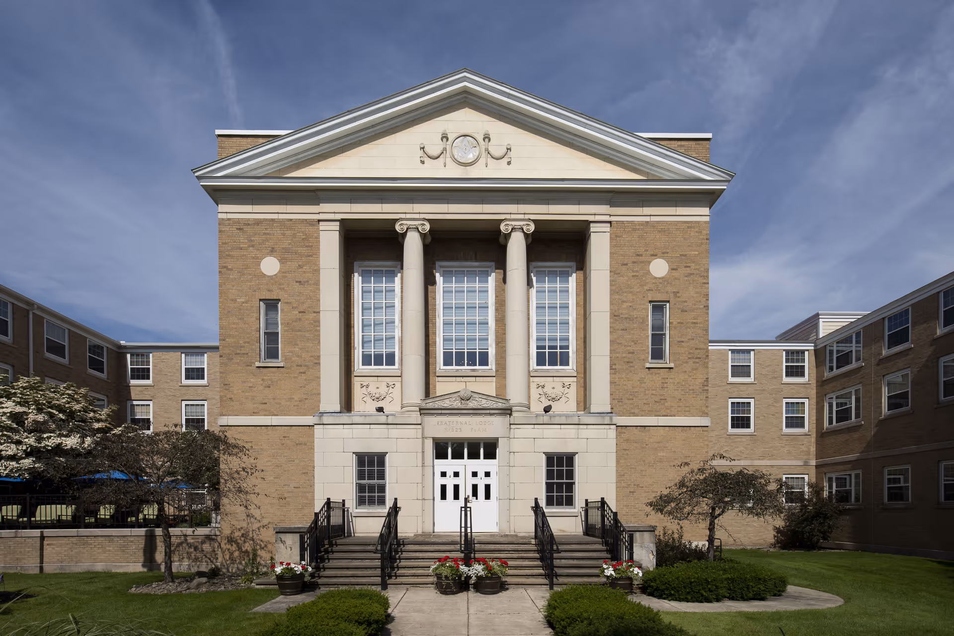 Front facade of a brick institutional-style building with tall columns, a pediment, and steps leading to double entrance doors.