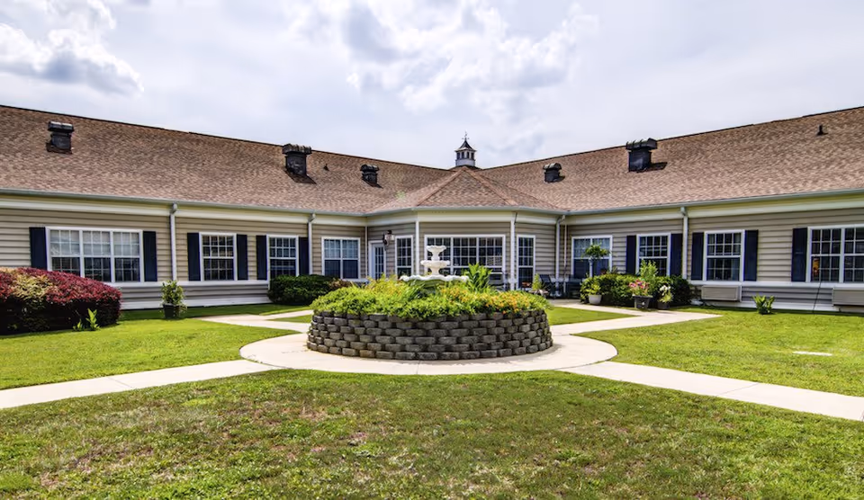 U-shaped single-story senior living building surrounding a grassy courtyard with a circular raised flower bed and fountain.