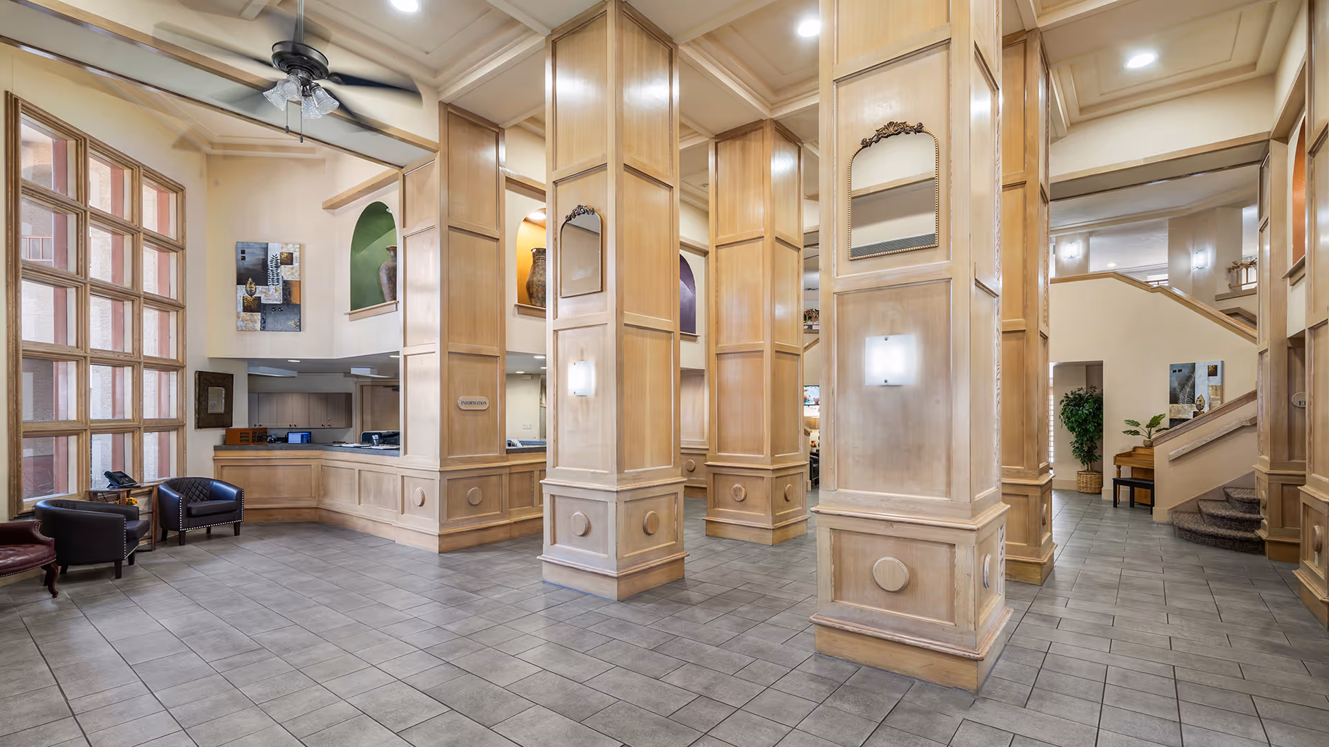 Spacious senior living lobby with tall wooden columns, a reception desk, seating area, and tiled floor.
