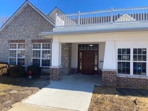 Front entrance of a low-rise brick and stone building with a covered porch, double wooden doors, and windows.