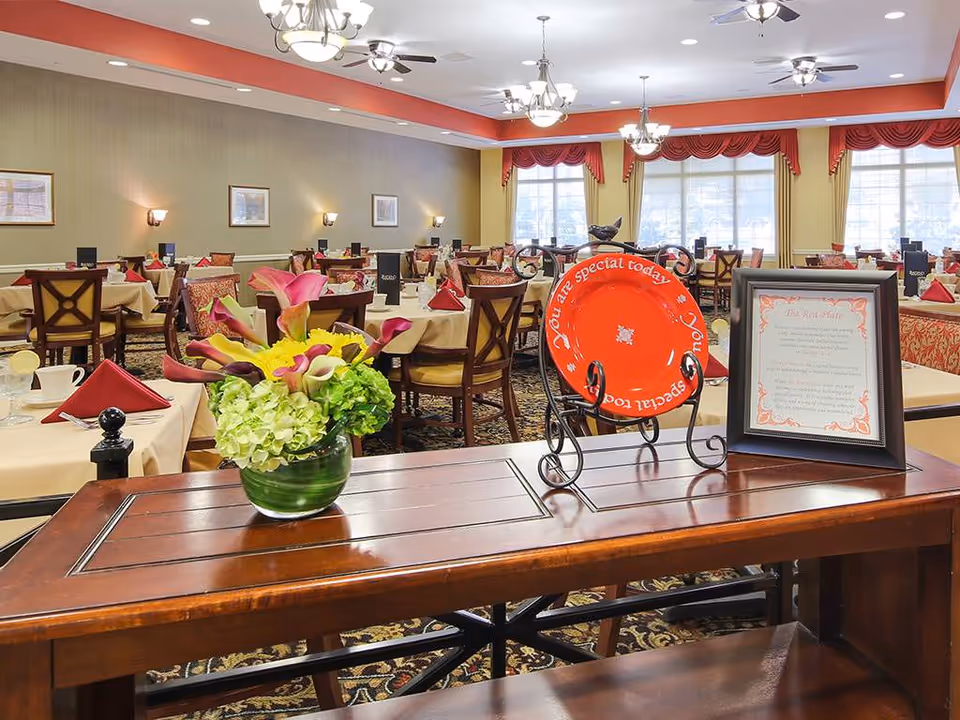 Spacious dining room with multiple set tables, a floral centerpiece on a wooden sideboard and a decorative red plate on display.