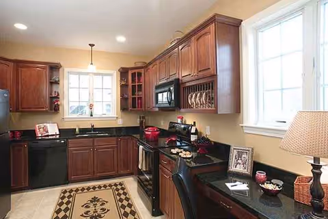 A well-equipped kitchen with dark countertops, wooden cabinets, appliances, and a windowed corner.