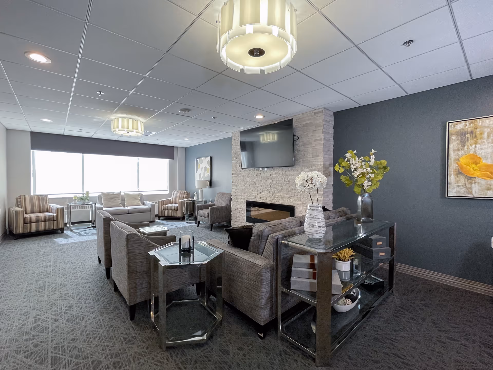 Spacious modern lounge with sofas and armchairs arranged around a fireplace and wall-mounted TV, with glass tables and decorative plants.