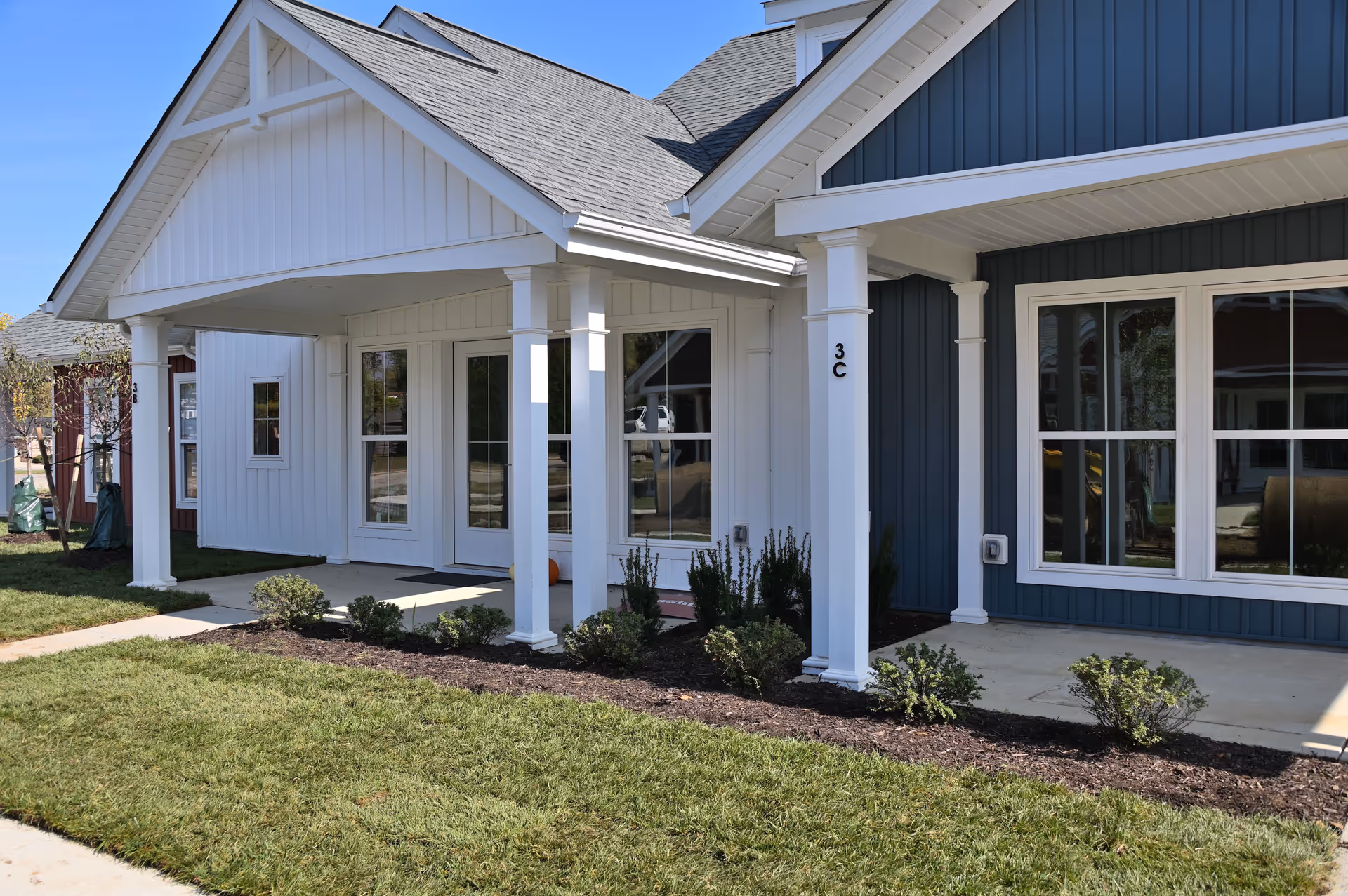 Front exterior of a single-story senior living unit with a covered porch, white columns, and blue and white siding.