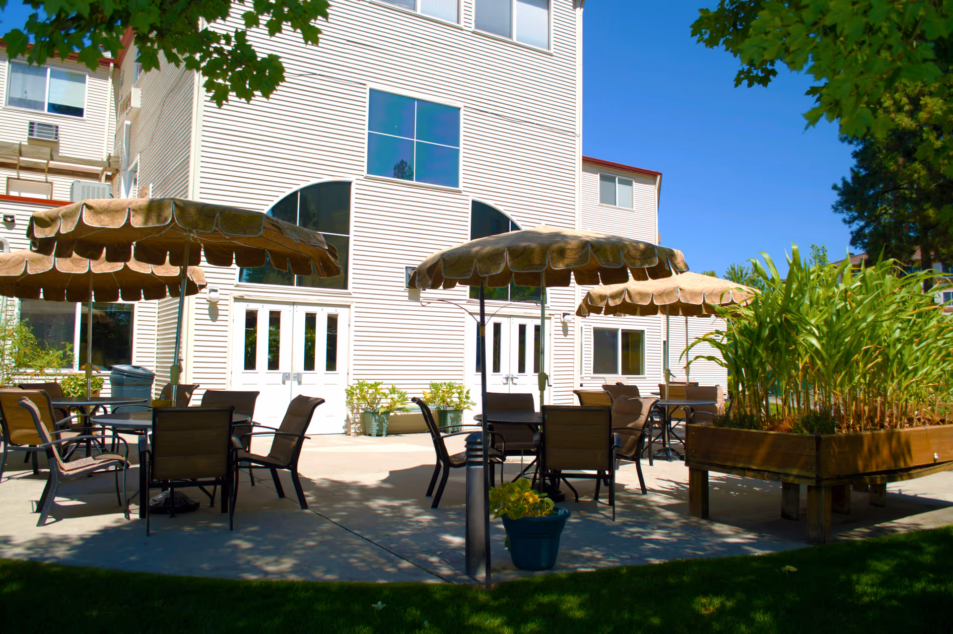 Outdoor patio with tables, chairs, and umbrellas in front of a multi-story senior living building.