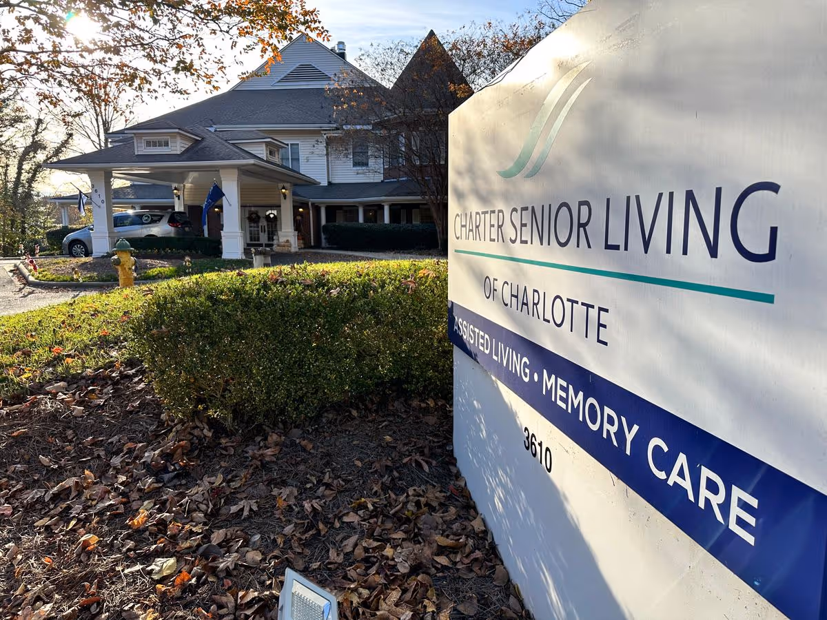 Entrance of Charter Senior Living of Charlotte with a large facility sign in the foreground and the building's covered driveway and landscaping in the background.