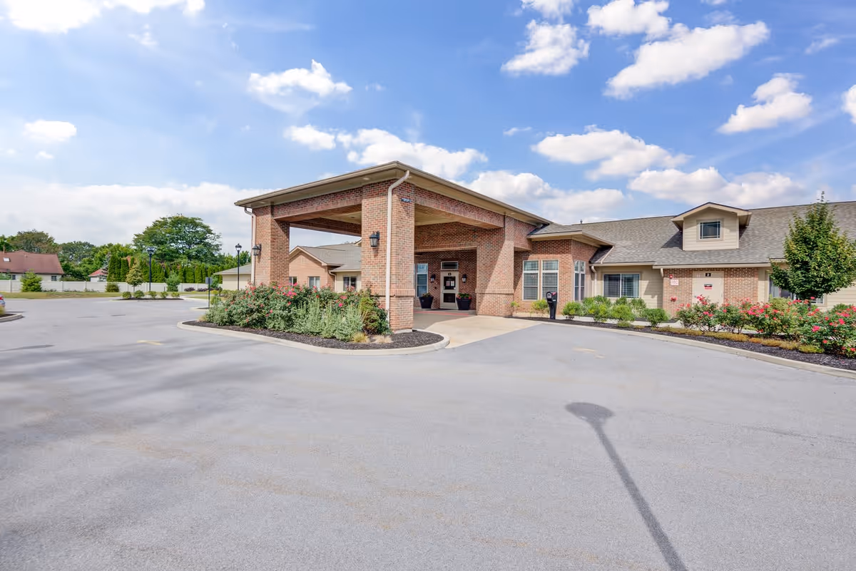 Exterior view of a single-story brick building with a covered entrance and landscaped flower beds under a partly cloudy sky.