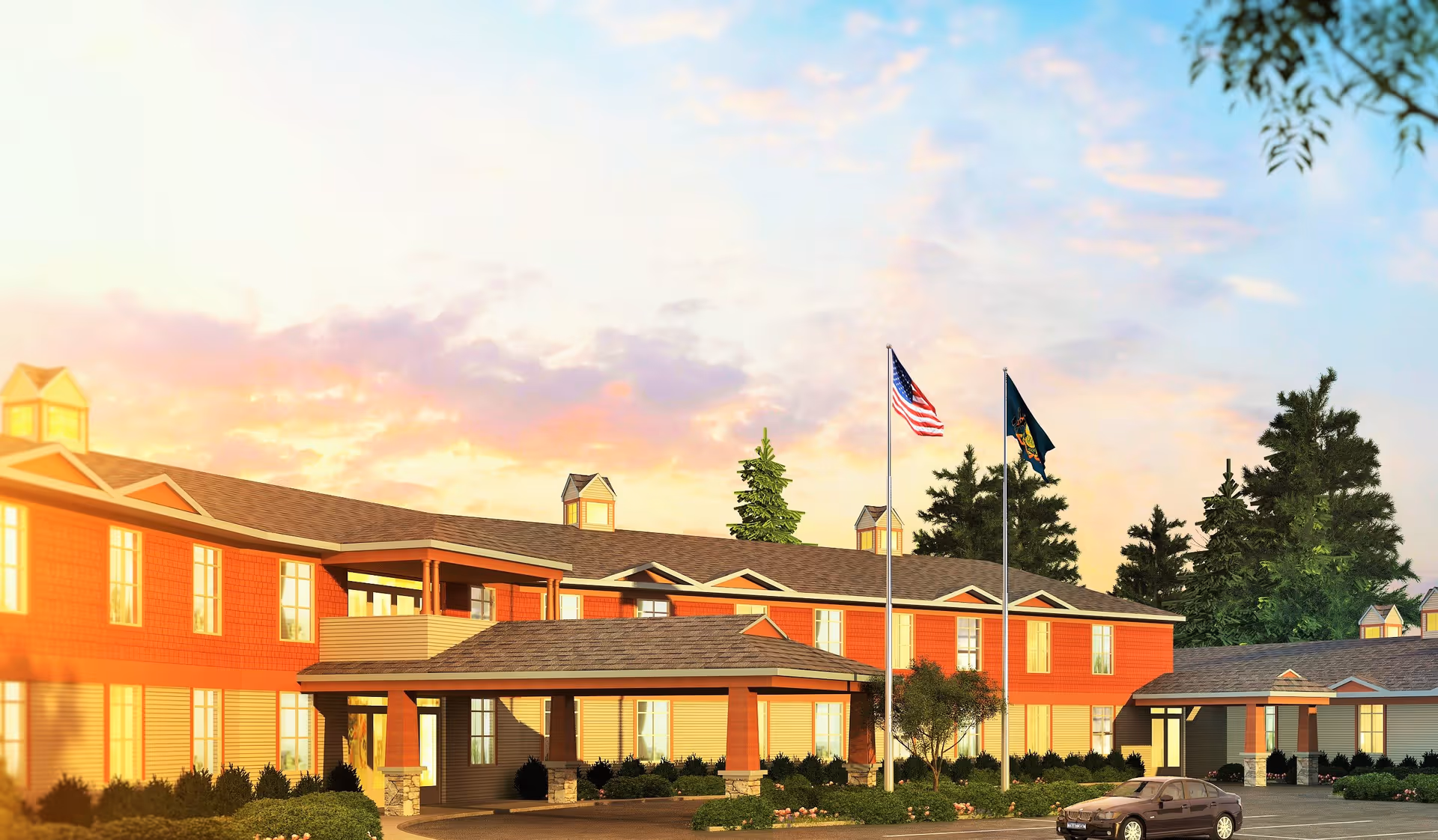 Exterior view of The Pines Senior Living facility during sunset with a two-story building featuring red and beige siding, multiple windows, a covered entrance, two flagpoles with the American flag and another flag, surrounded by trees and landscaping, and a parked car in the driveway.