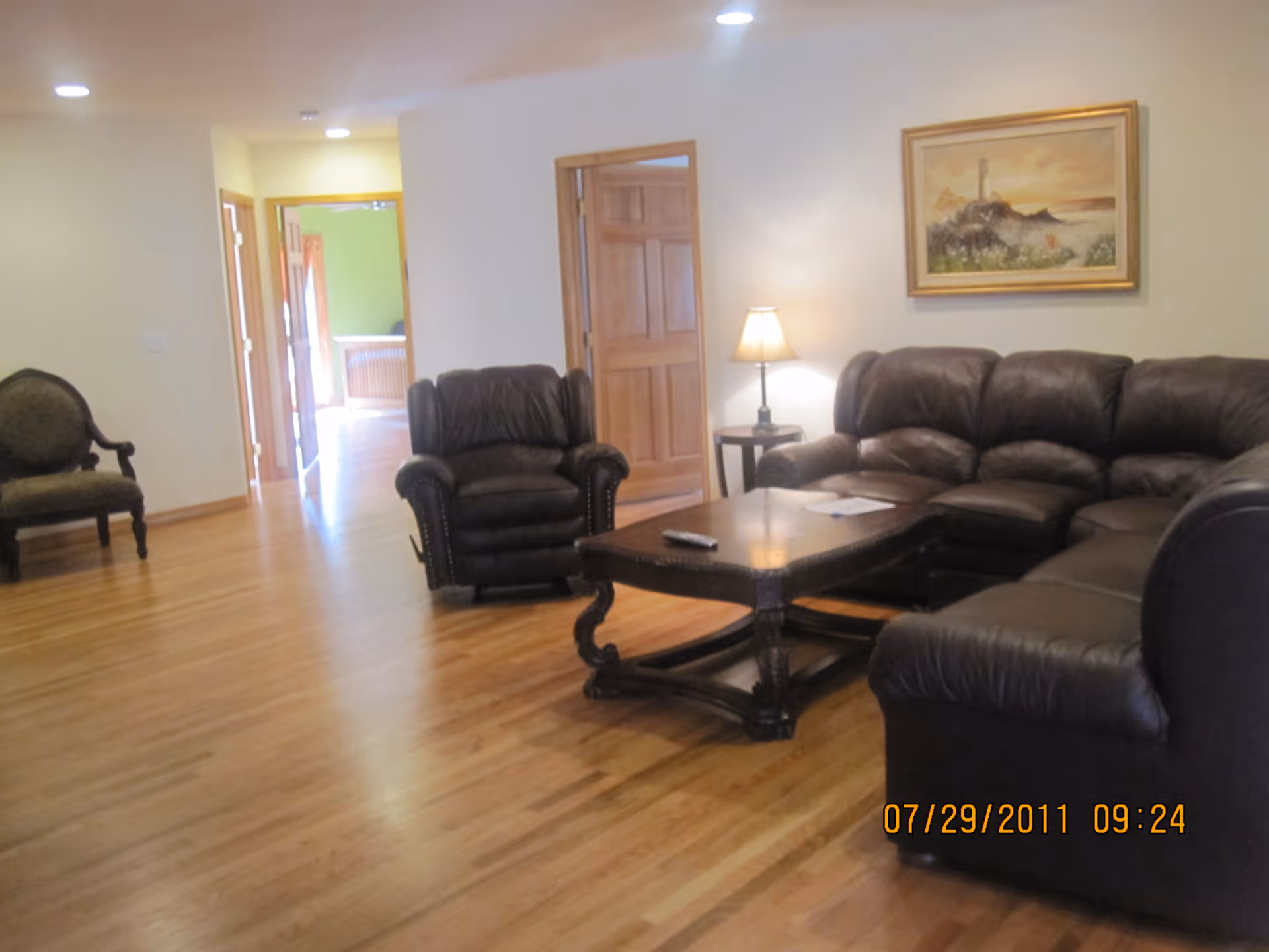 Spacious living room with a leather sectional and armchair around a wooden coffee table on hardwood floors.