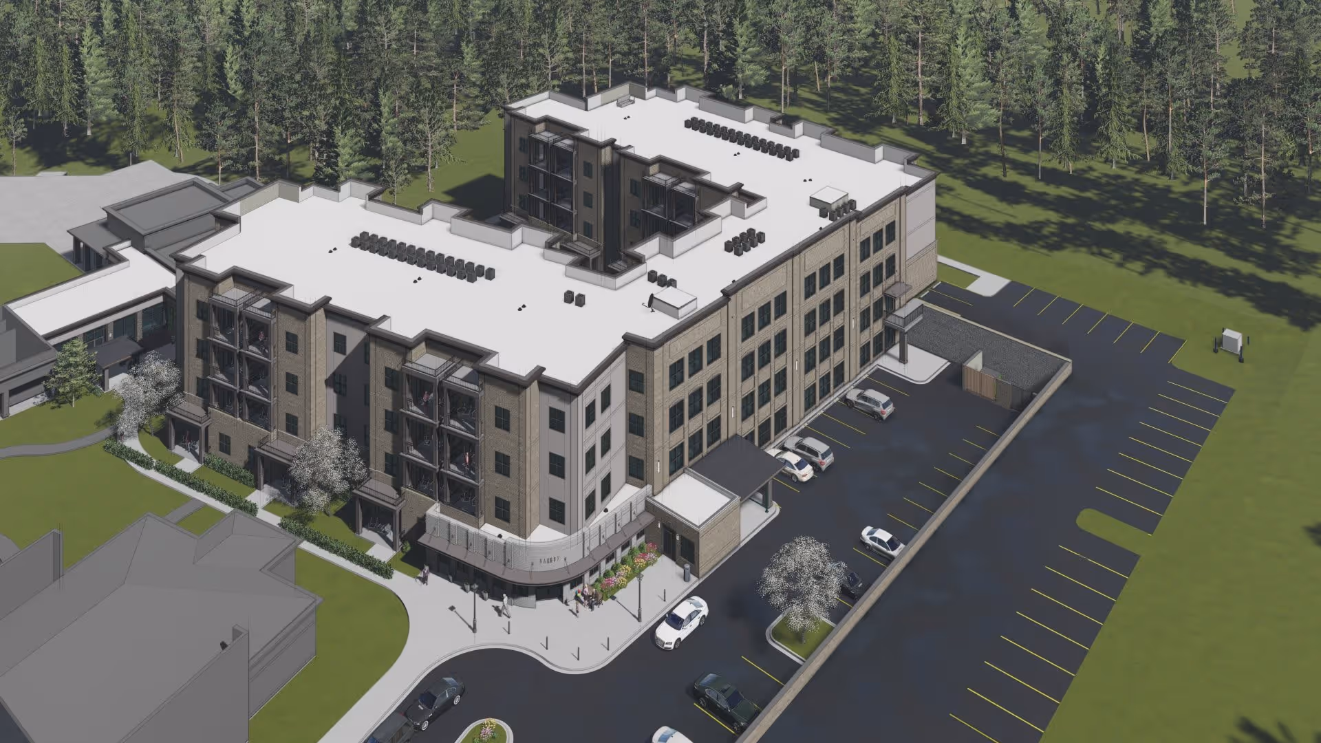 Aerial view of a multi-story senior living facility building surrounded by parking spaces and greenery, with a forested area in the background.