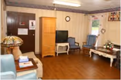 Small common room with chairs, a TV on a stand, a wooden cabinet, coffee table with flowers, and hardwood flooring.