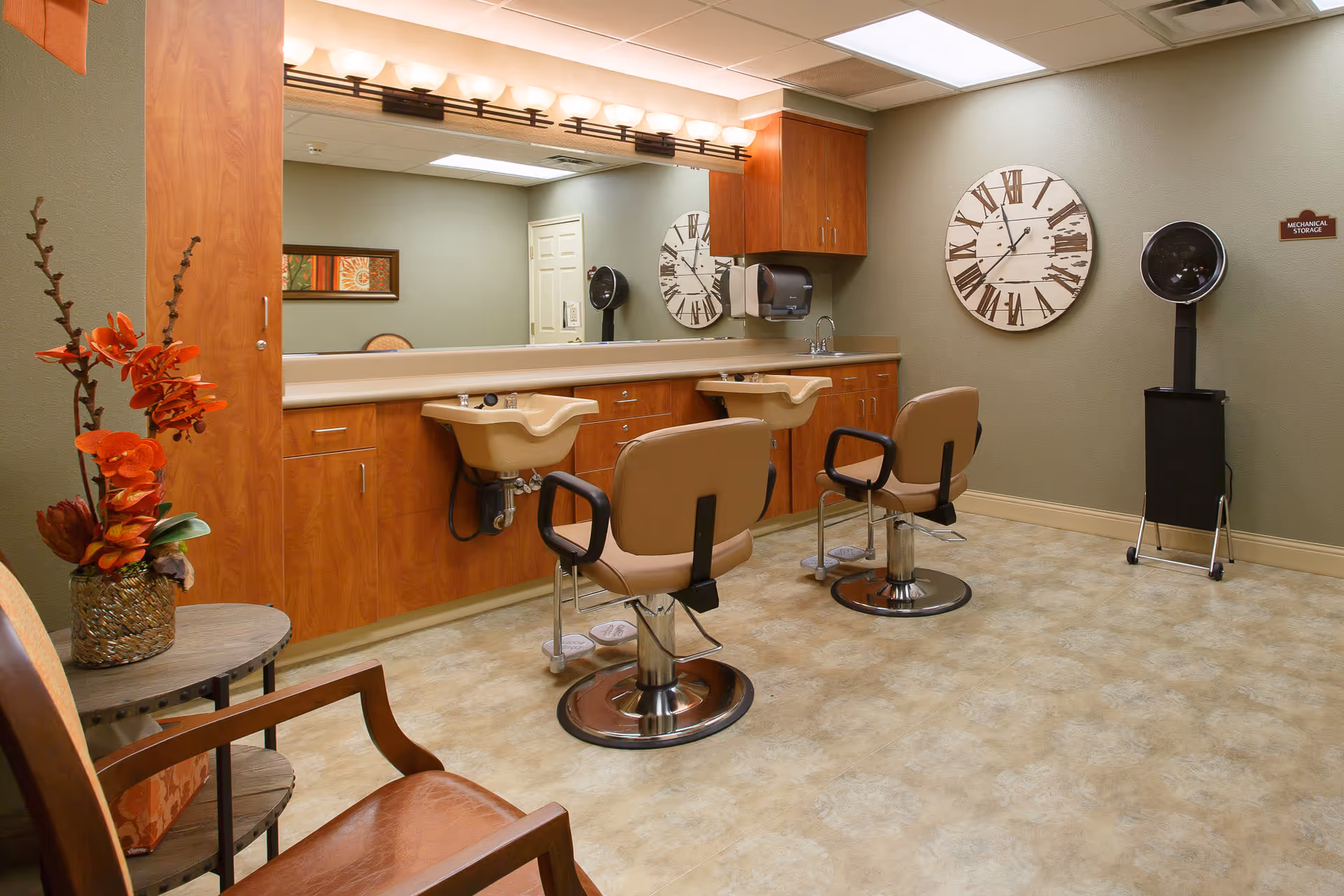 Hair salon room with two styling chairs, shampoo sinks, a large mirror, wooden cabinets, and a wall clock.