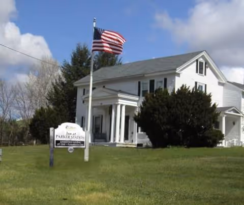 White two-story building with flagpole and manicured lawn in front, Inn at Parker Station sign.