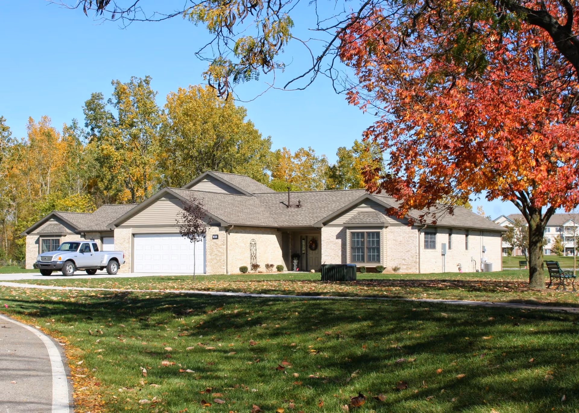 Single-story brick building with an attached two-car garage, a pickup truck in the driveway, and autumn trees and lawn in front.