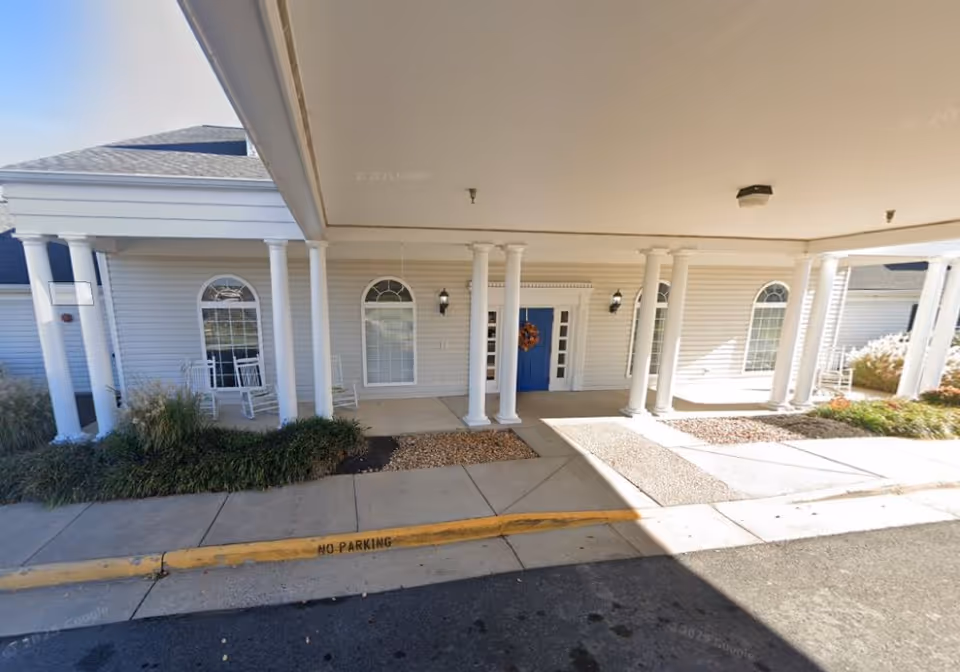 Exterior view of Cambridge Landing Memory Care entrance with pillars, a blue door, and seating.