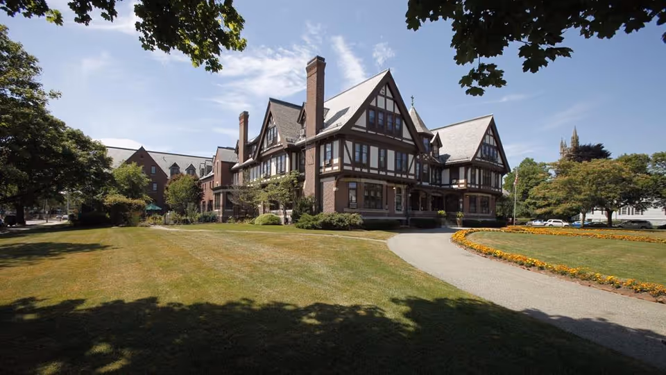 Exterior view of a Tudor-style senior living facility with a curved driveway and manicured lawn.