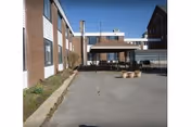 Outdoor paved area beside a brick building with a covered seating area featuring tables and chairs, under a clear blue sky.