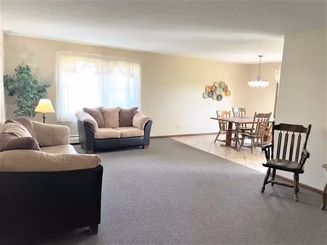 Bright open living and dining room with two sofas, a floor lamp, a dining table and chairs, and neutral decor.