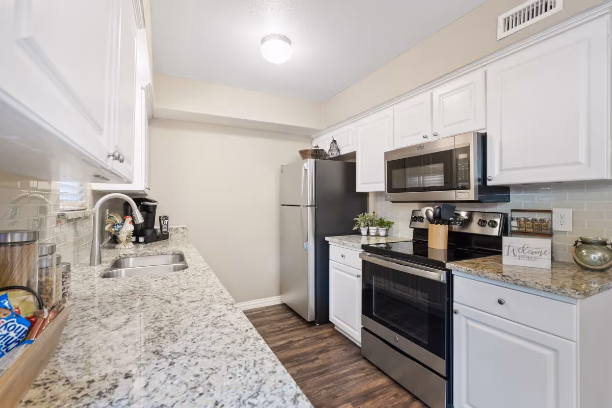 Modern kitchen with white cabinets, granite countertops, a stainless-steel fridge, stove, and microwave.