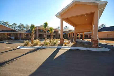 Exterior view of Partin Place Senior Living showing the entrance with a covered drop-off area, palm trees, and landscaped plants under a clear sky.