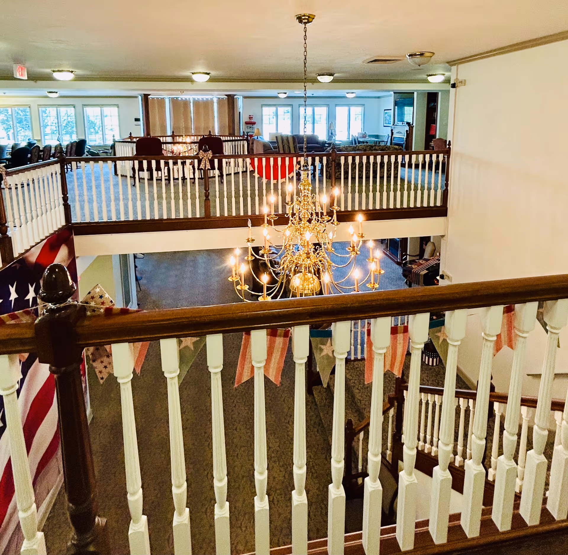 View over a second-floor railing into a decorated lobby with a large chandelier and seating areas.