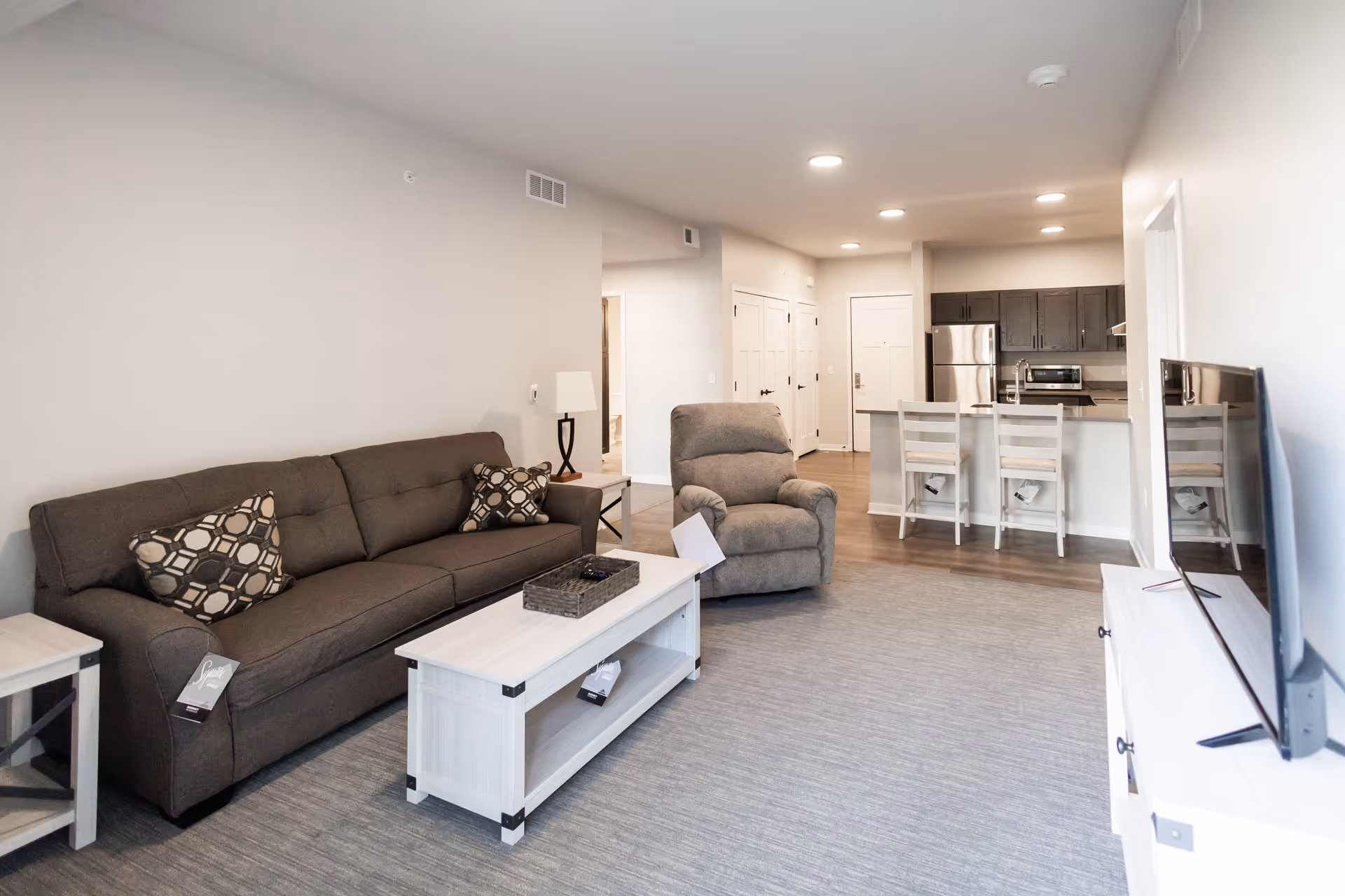 Open-plan living room with a sofa, recliner, coffee table and a kitchen with a breakfast bar and stools in the background.