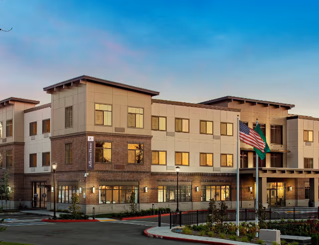 Exterior view of Jefferson House Memory Care Community building with flags and landscaped entrance.