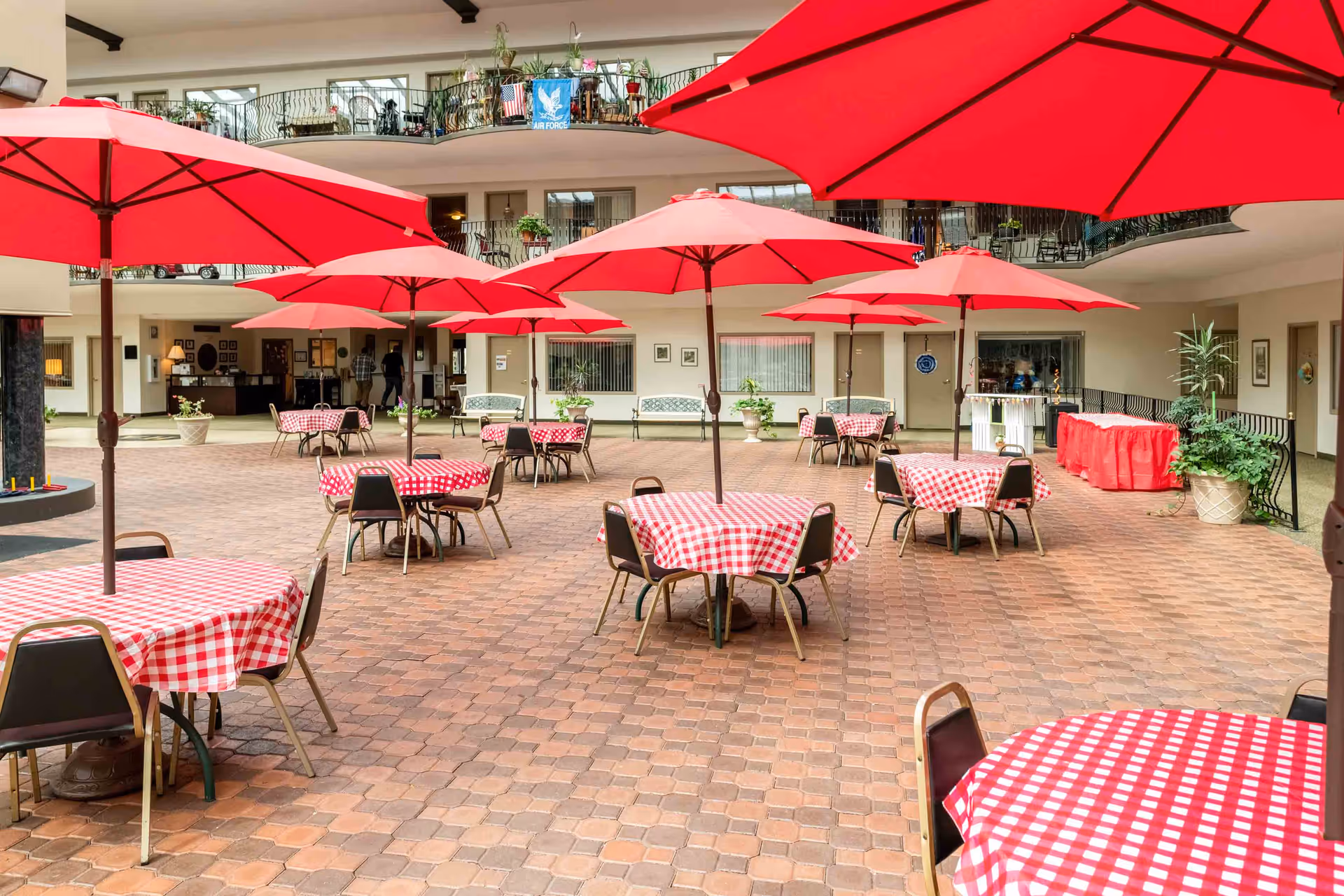 Indoor atrium with red umbrellas and round tables covered in red-and-white checkered tablecloths.