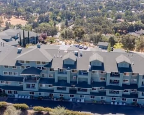 Aerial view of a multi-story building with balconies surrounded by trees and hillside landscape.