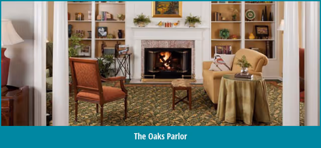 Cozy parlor with a lit fireplace flanked by built-in bookshelves, upholstered chairs, a sofa, and a small round table.