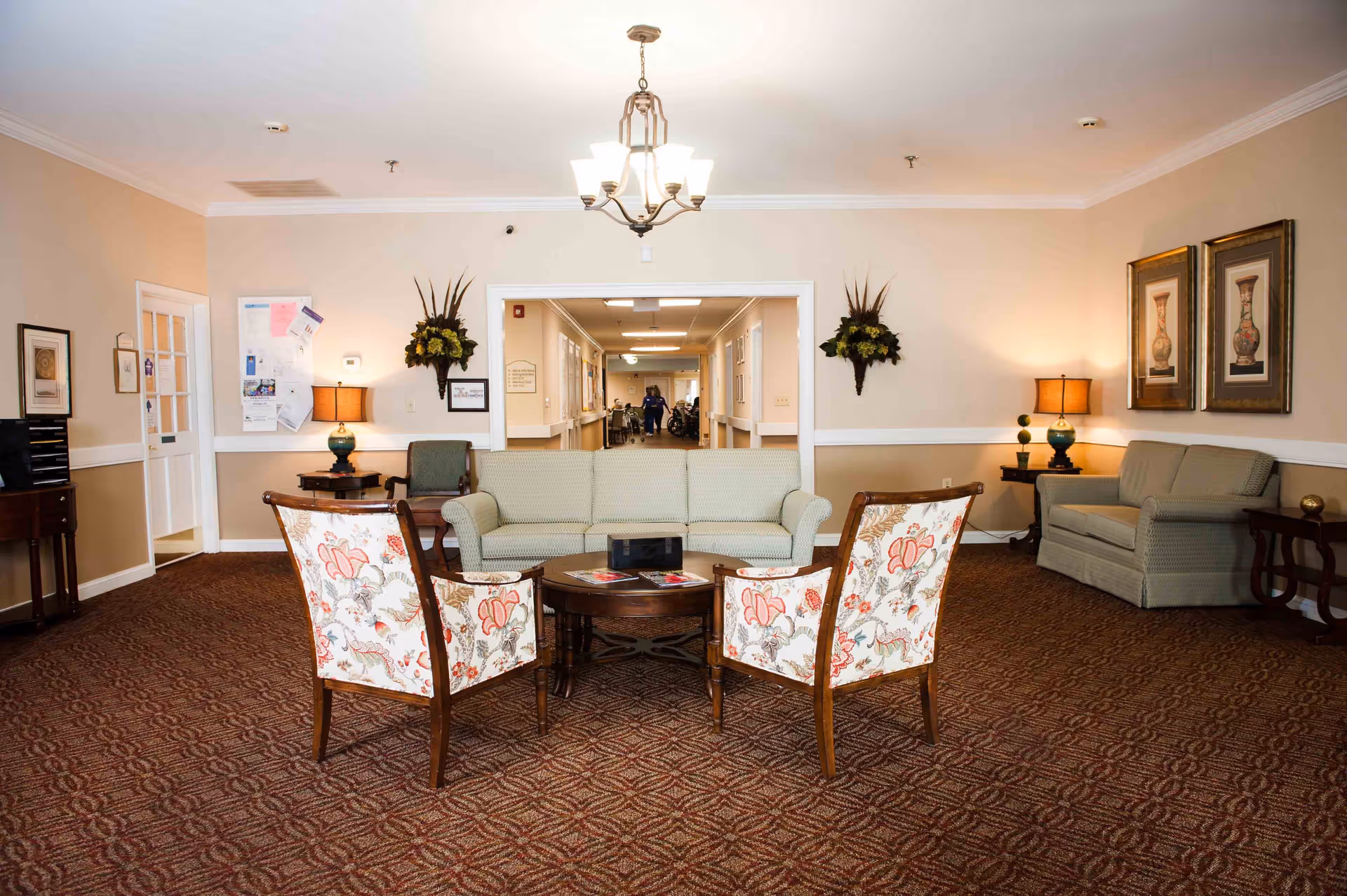 Comfortable lobby-style sitting area with sofas, floral armchairs, a central coffee table, and a hallway beyond.