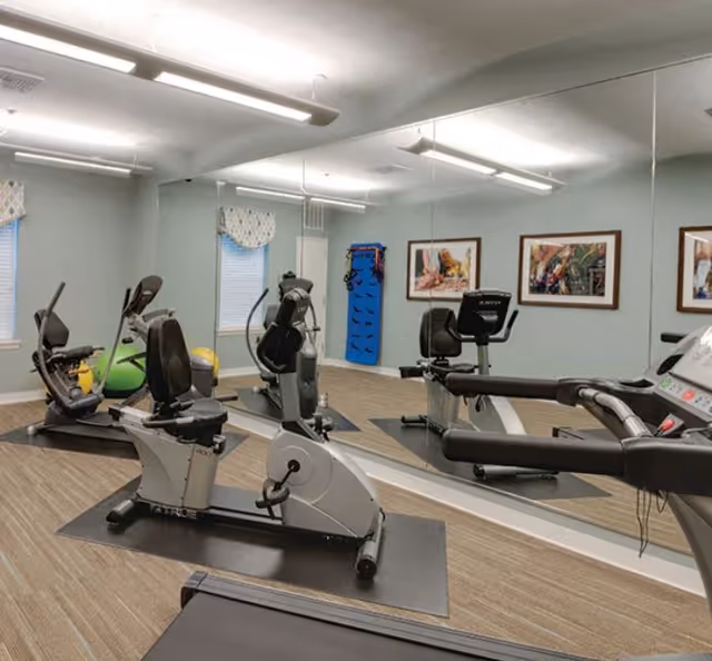 Interior fitness room with recumbent exercise bikes, a treadmill, mirrored wall, and fitness equipment.