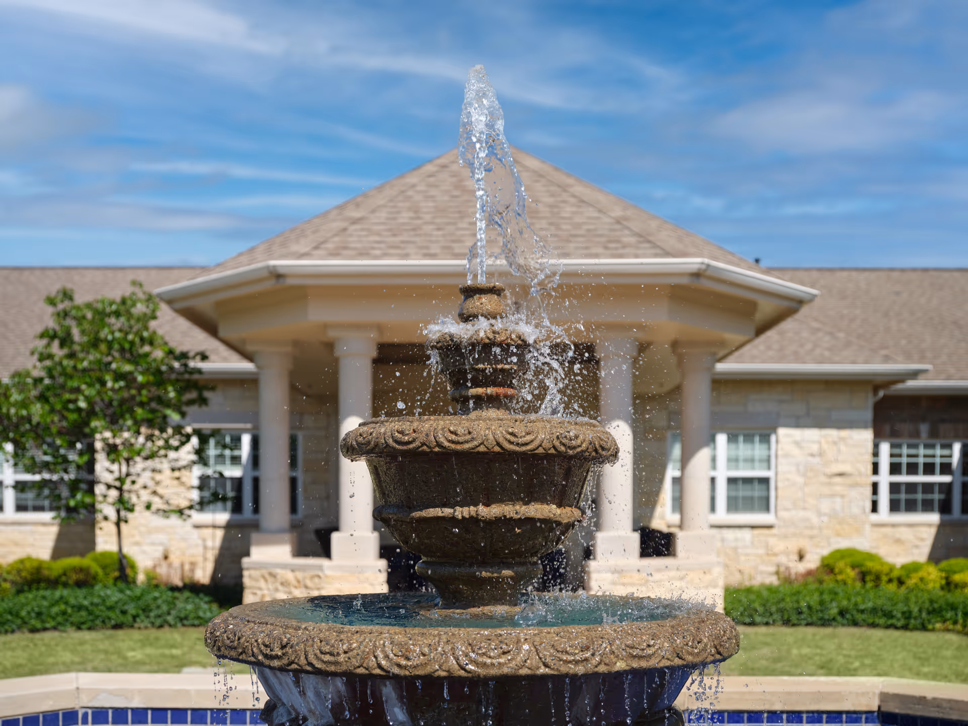 Stone tiered fountain in front of a memory care facility with a columned entrance.