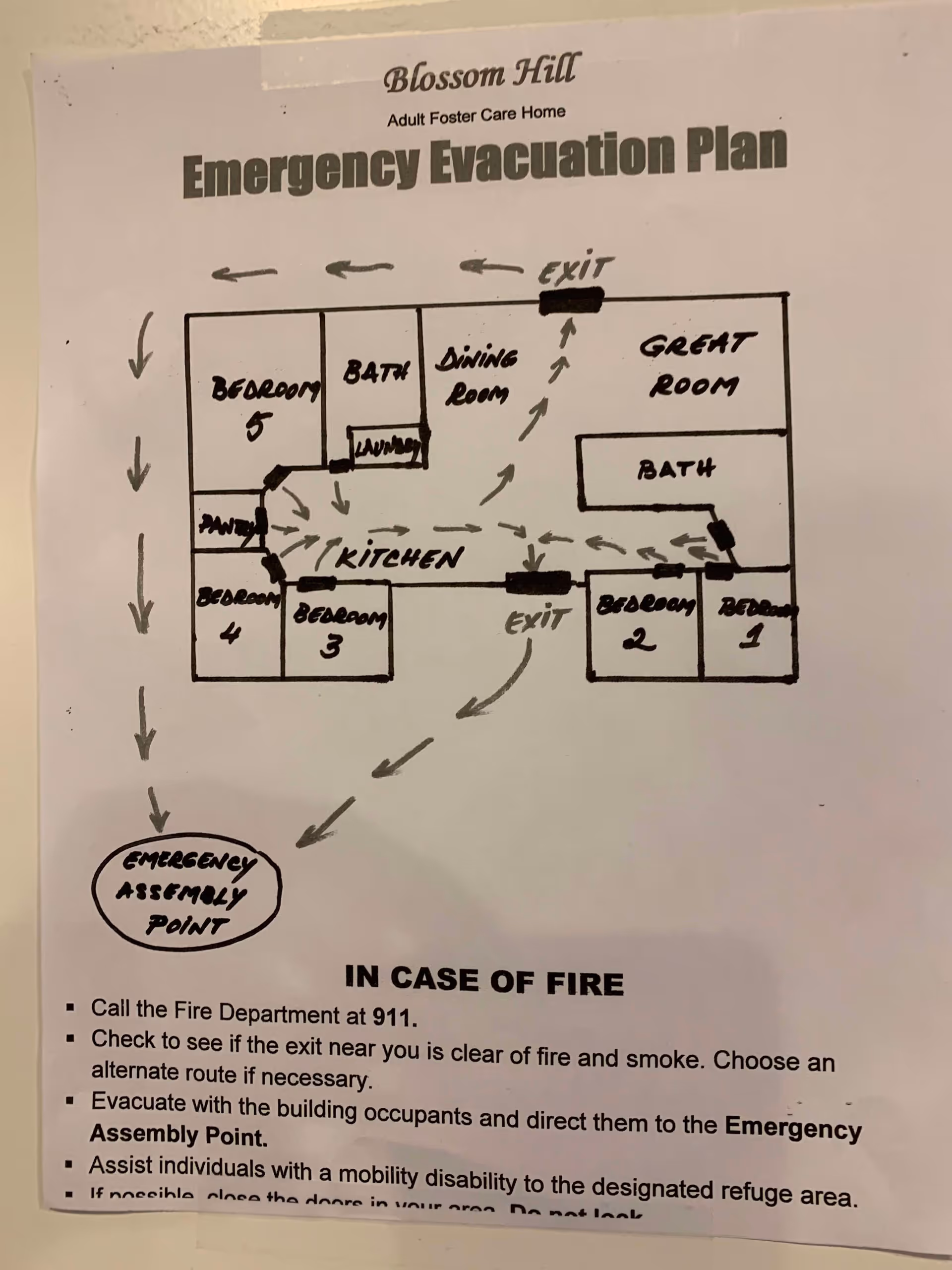 Emergency evacuation plan for Blossom Hill Adult Foster Care Home showing a hand-drawn floor layout with labeled rooms including bedrooms, baths, kitchen, dining room, great room, pantry, and laundry. Arrows indicate evacuation routes leading to exits and an emergency assembly point. Instructions for fire emergencies are listed below the map.