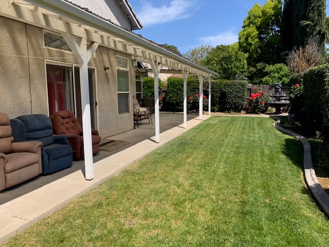 A sunny backyard with a covered patio, lawn, outdoor seating and a small fountain.