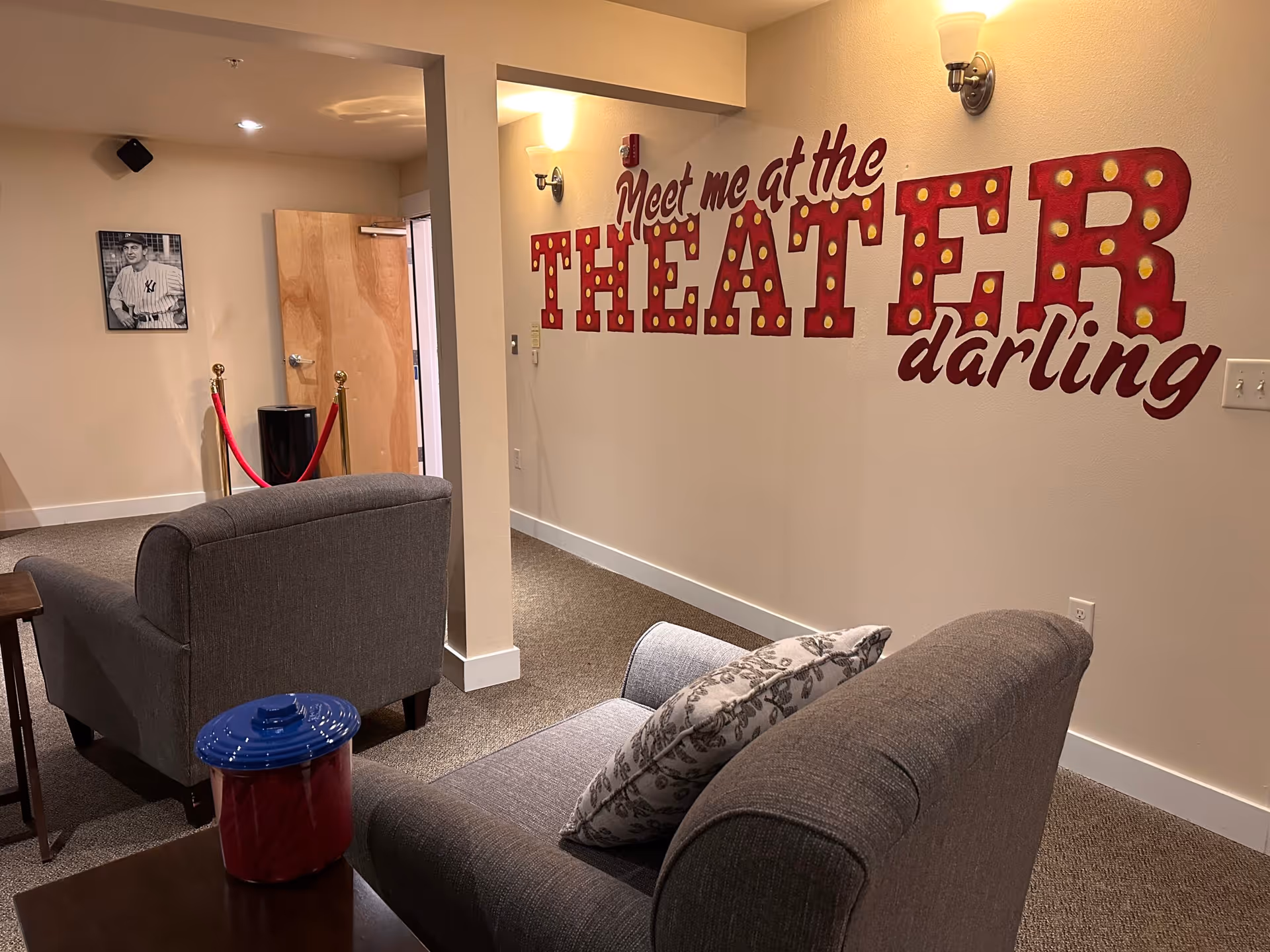 A cozy lounge area with gray sofas and a bold theater-themed mural on the wall.