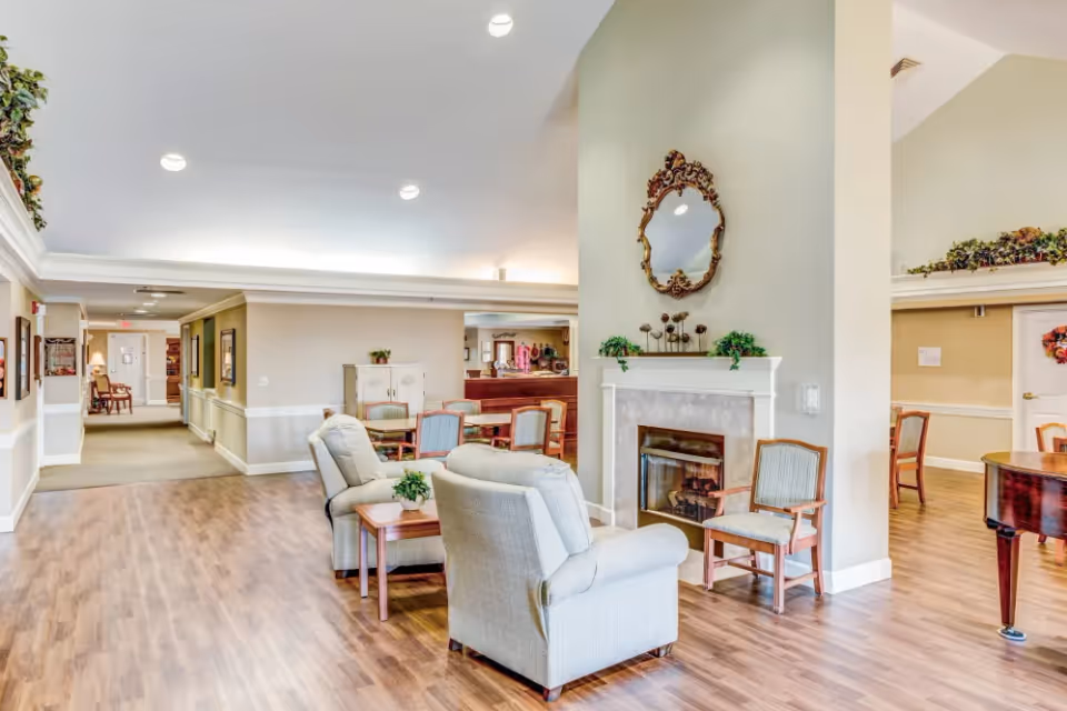 Spacious senior living common area with armchairs, a fireplace, dining tables and wood flooring.