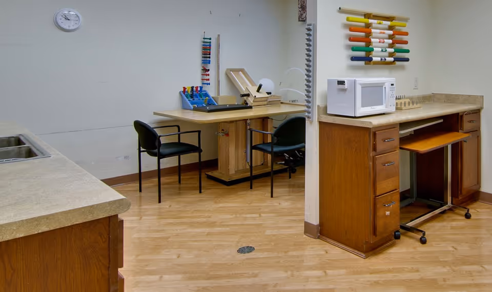 An interior multipurpose room with counters, a microwave and sink, chairs around a work table, and colorful activity tools mounted on the wall.