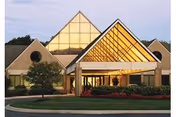 Front view of a senior living center with pyramid-shaped glass entry and manicured landscaping.