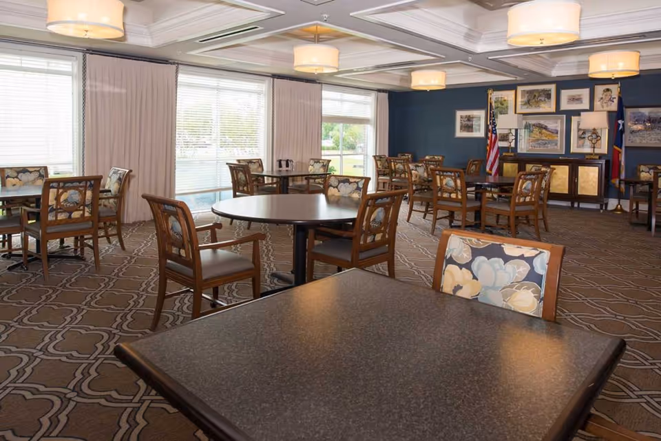 Well-lit dining room with round and square tables and floral-upholstered chairs.
