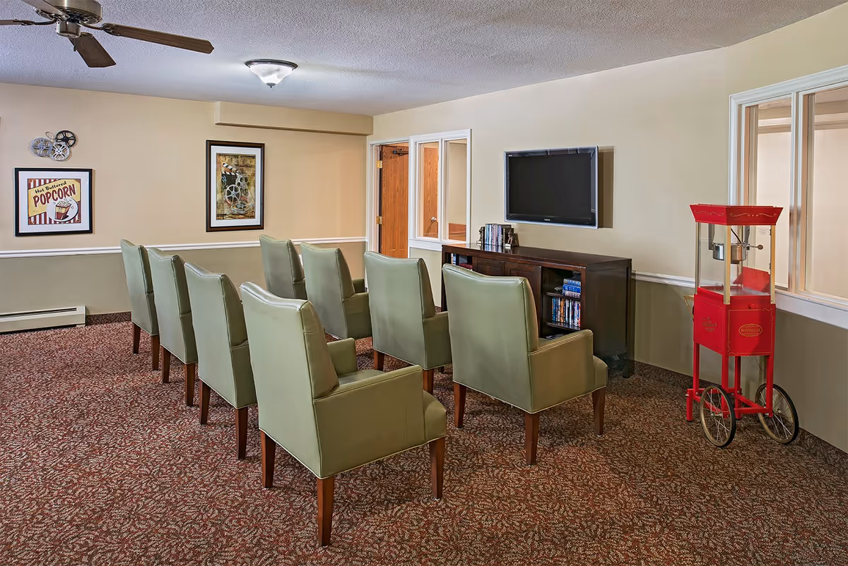 Small screening room with two rows of green armchairs facing a wall-mounted TV, a wooden media console, and a red popcorn machine.