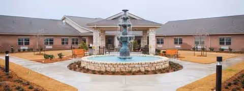 Outdoor courtyard with a central fountain, surrounding benches, and a brick facility building in background.