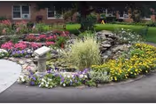 Outdoor garden with colorful flowers and a stone path in front of brick senior care building.