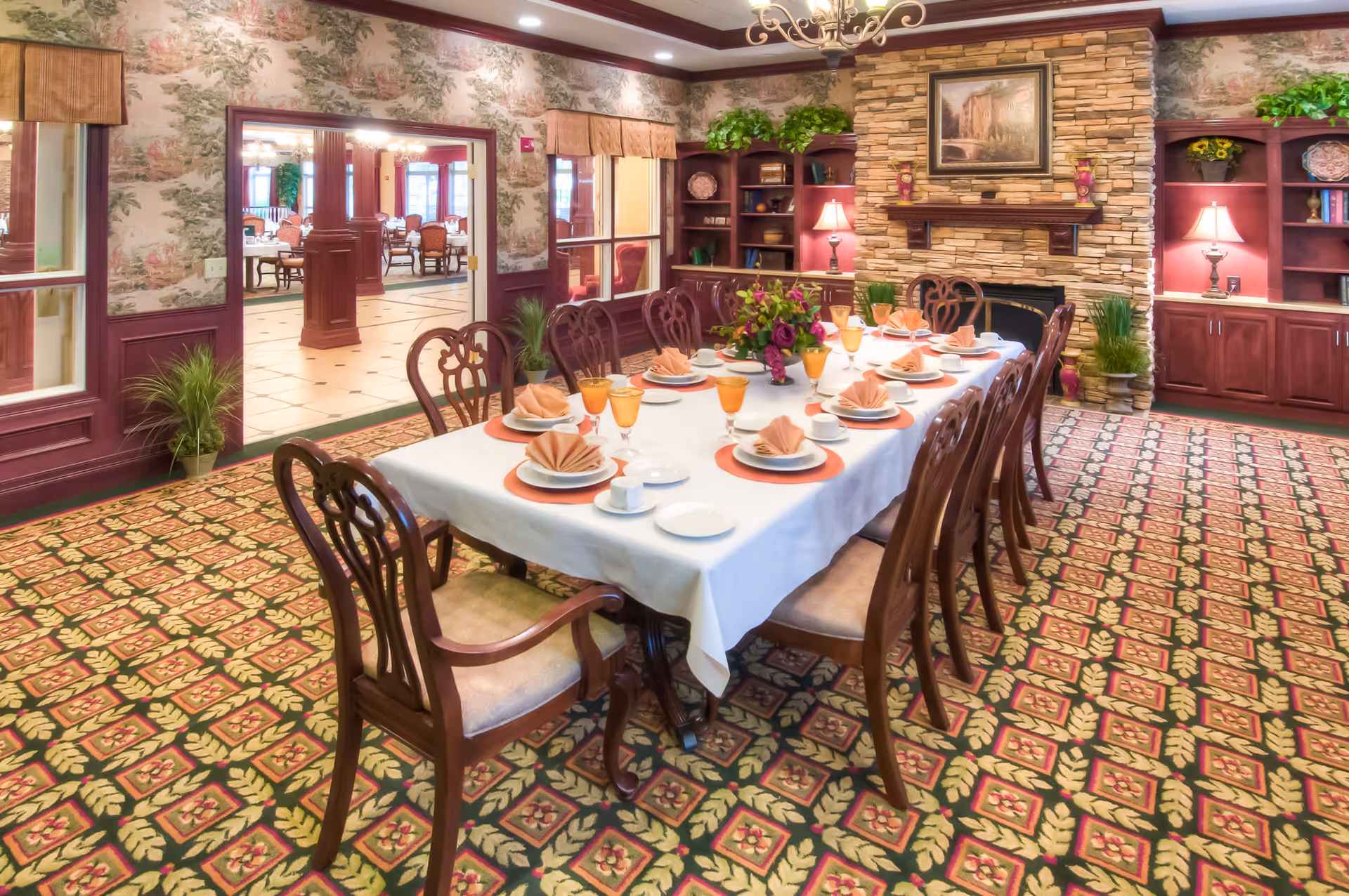 Elegantly set dining table with chairs in a decorated dining room featuring built-in shelves and a stone fireplace.