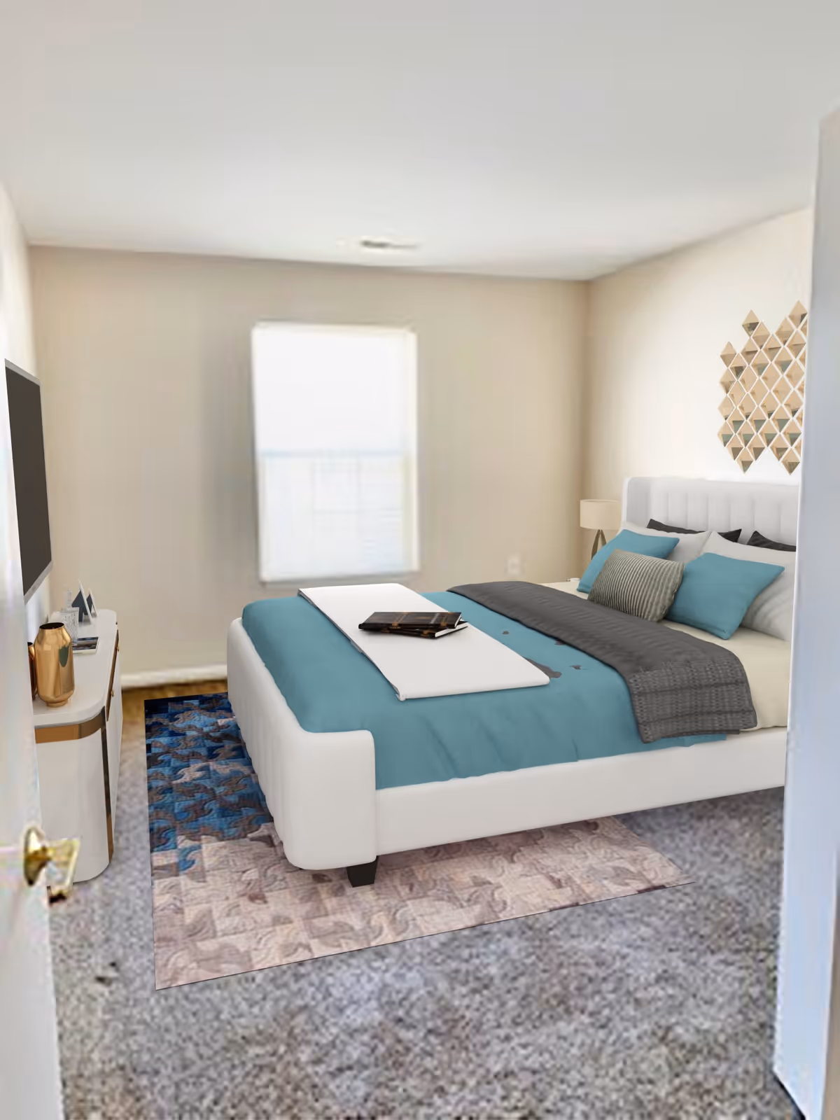 A bedroom with a white upholstered bed featuring teal and gray bedding, a patterned rug underneath, a window with a white blind, a small white dresser with decorative items, and a geometric wall decoration above the bed.