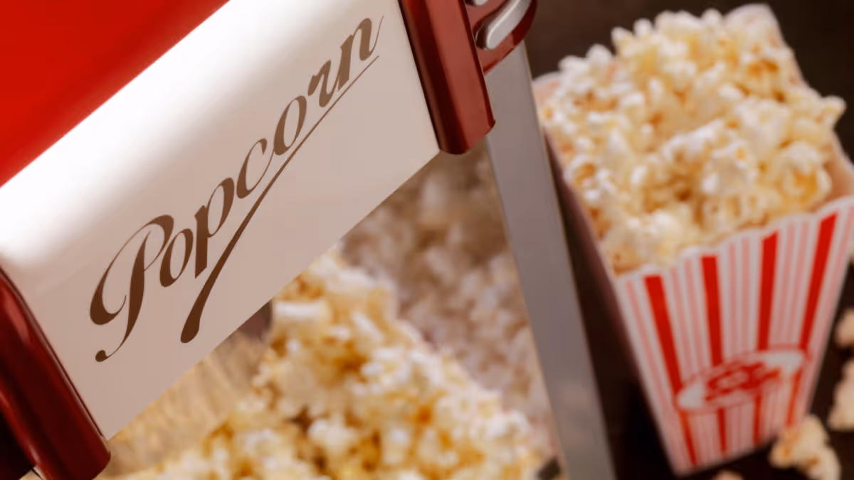 Close-up of a red and white popcorn machine with popped popcorn and a striped popcorn box.
