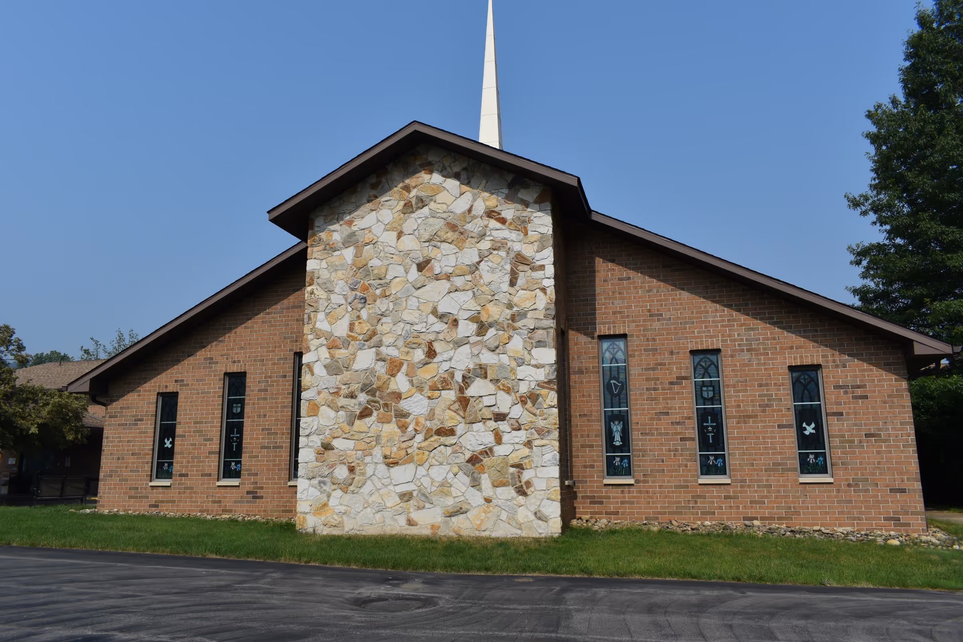 Brick building with a central stone facade, narrow stained-glass windows and a white steeple against a blue sky.