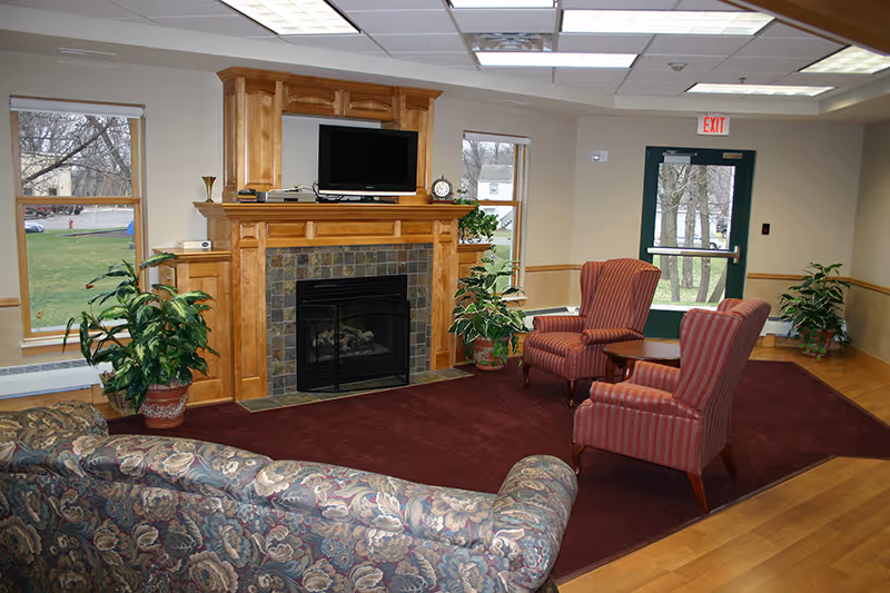 Comfortable common room with a fireplace and TV, a patterned sofa, two striped armchairs, and potted plants.