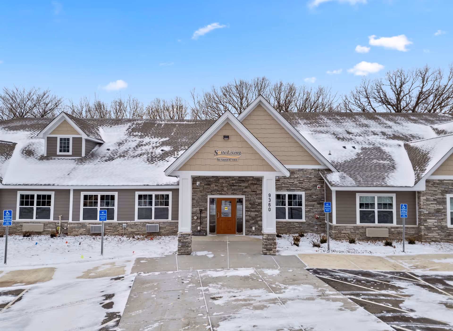 Front exterior view of Suite Living of Eden Prairie building with snow on the ground and roof, clear blue sky, and leafless trees in the background.