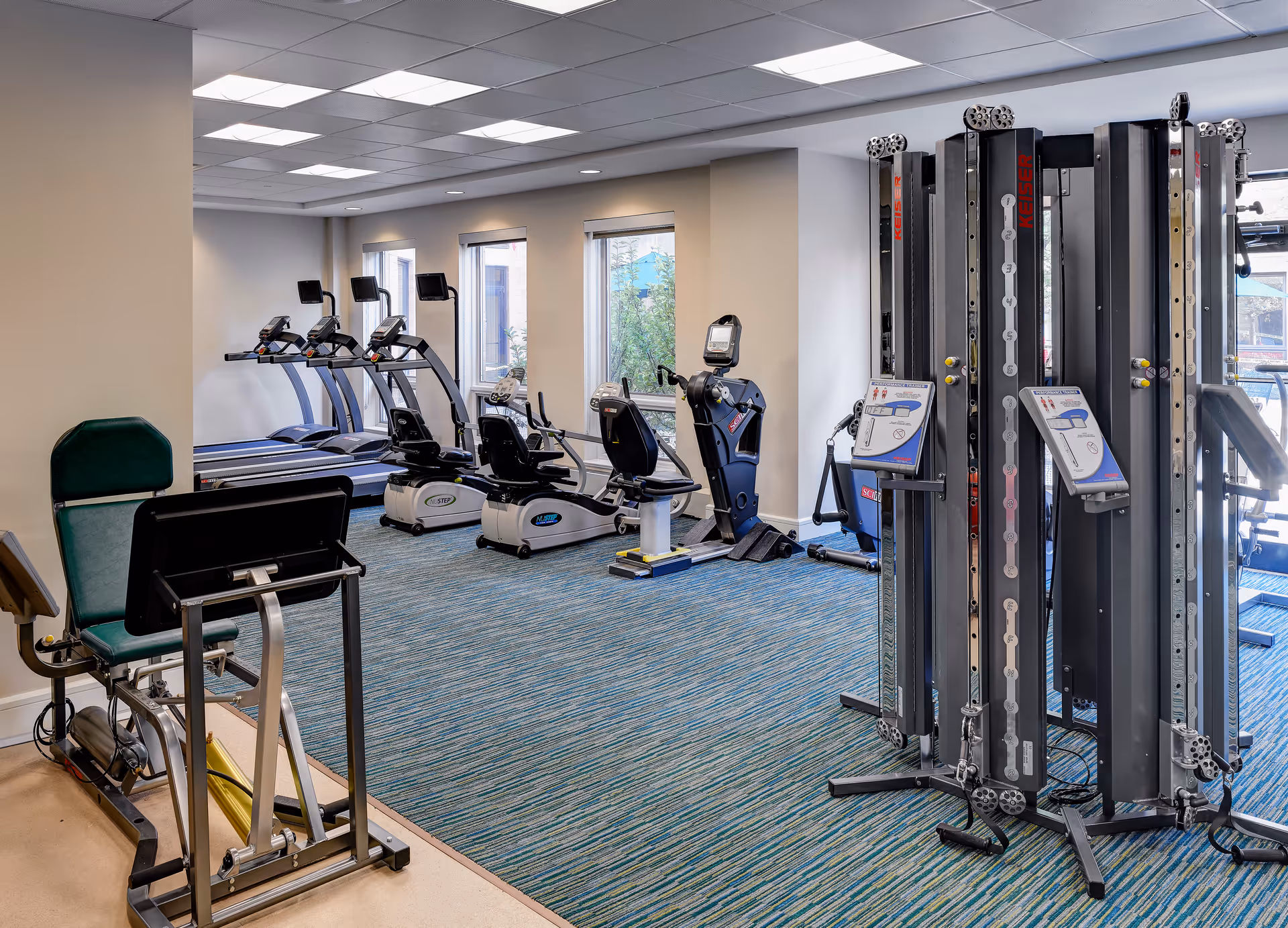 Well-equipped fitness room with treadmills, recumbent bikes, and weight machines on a teal-striped carpet.